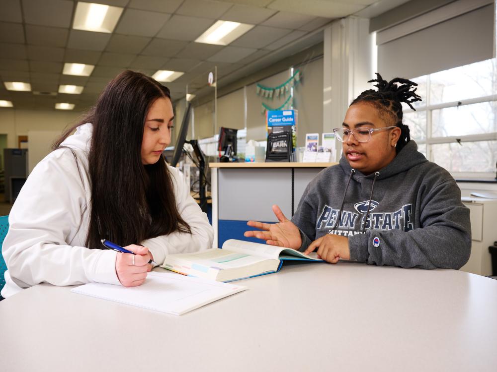 A student learner and tutor sitting at a table looking at a book