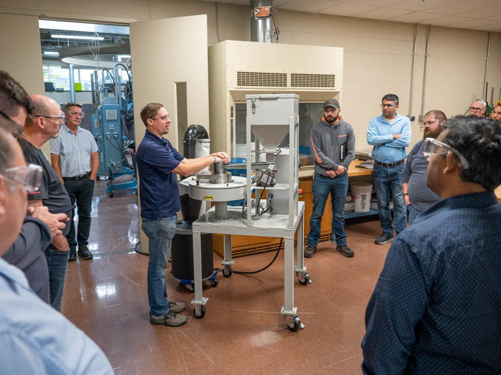 A group of people gather round a demonstration in a workshop.