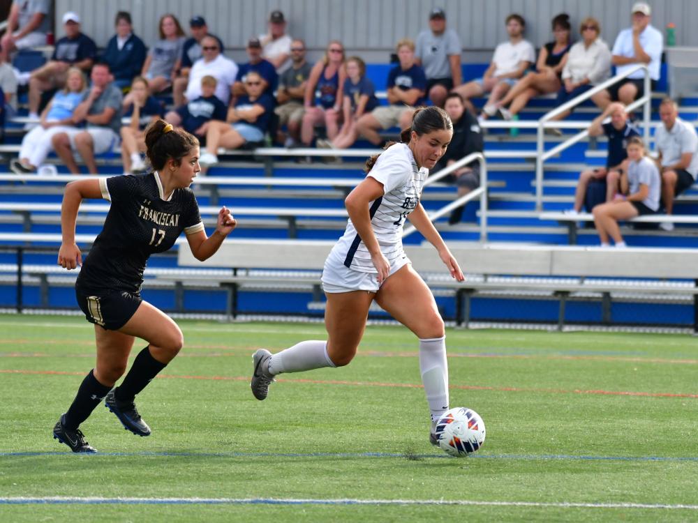 A Penn State Behrend soccer player advances the ball past a defender.