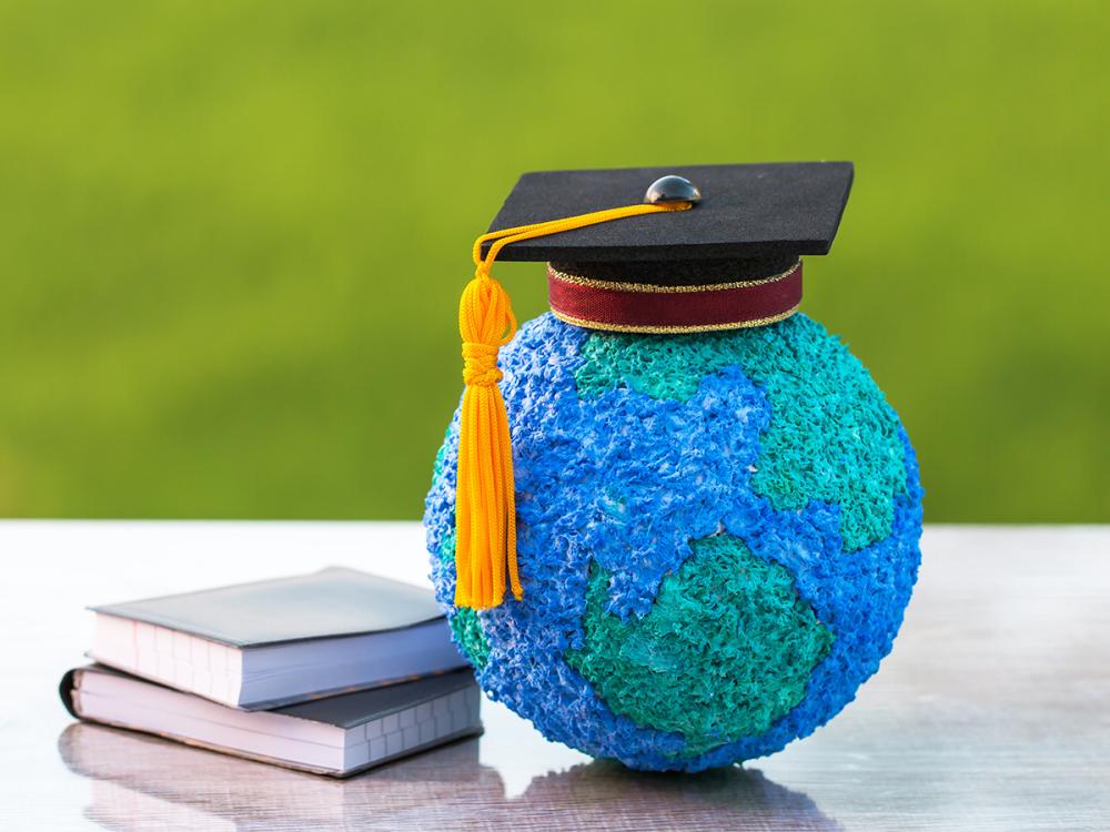 A small globe with a graduation cap on it sitting next to a pile of books