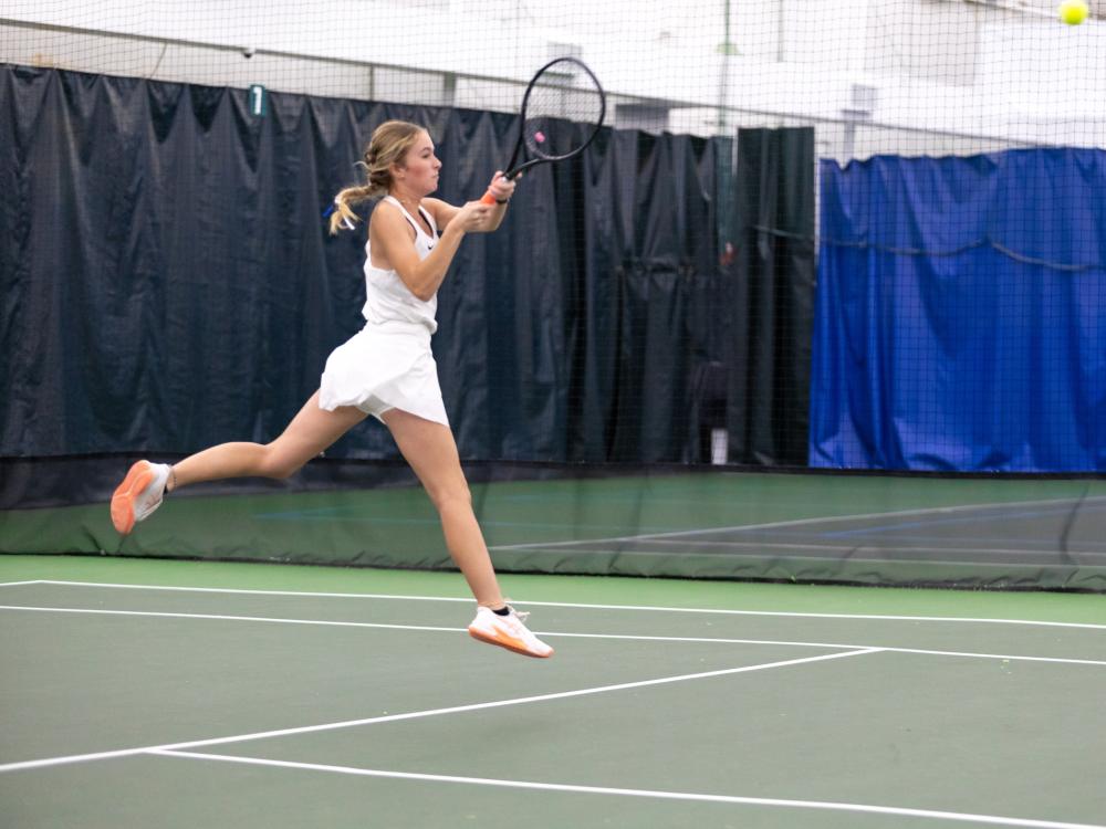 A Penn State Behrend tennis player jumps while hitting the ball.