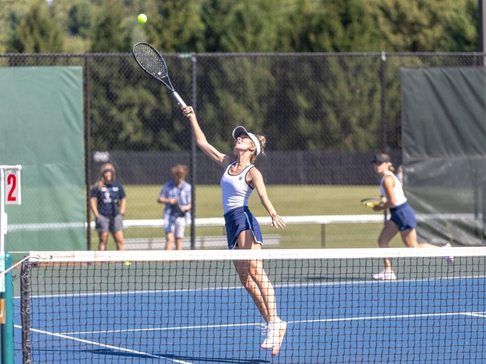 A member of the Penn State Behrend women's tennis team reaches up to hit a ball.