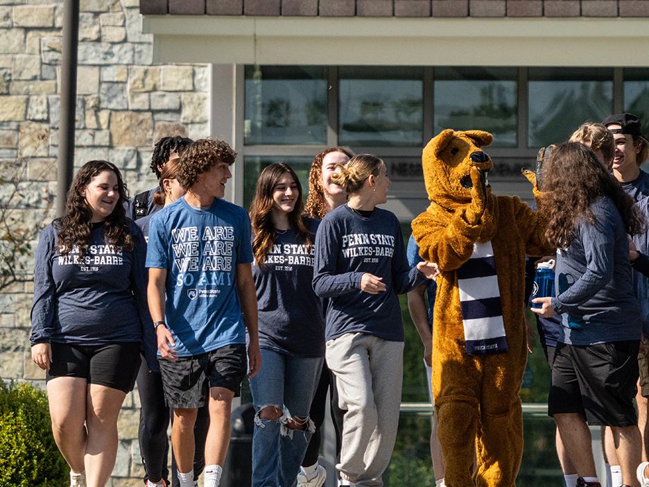 A group of students interacting with the Nittany Lion mascot outdoors.