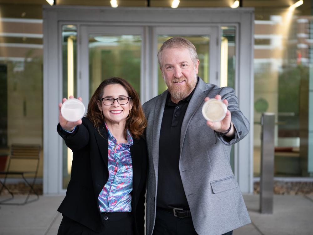 Image of two faculty members holding microbiome plates in front of the Millennium Science Complex