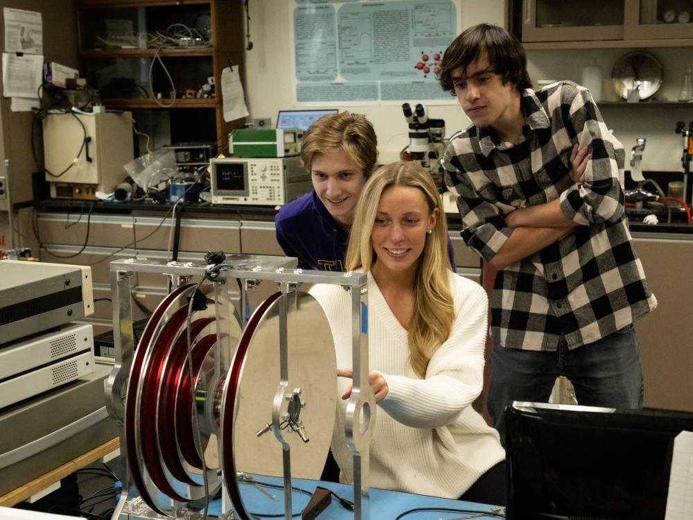 Three students lean over lab equipment. 