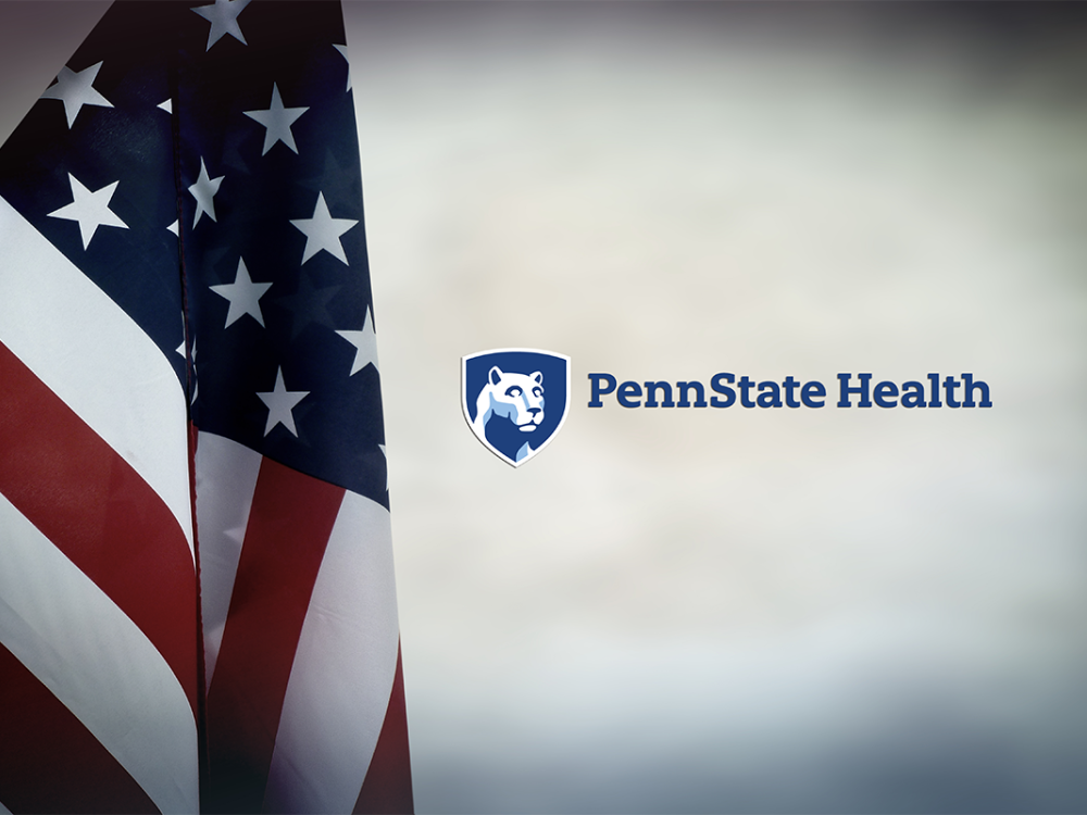 An American flag hangs down on the left, and to the right is the Penn State Health logo.