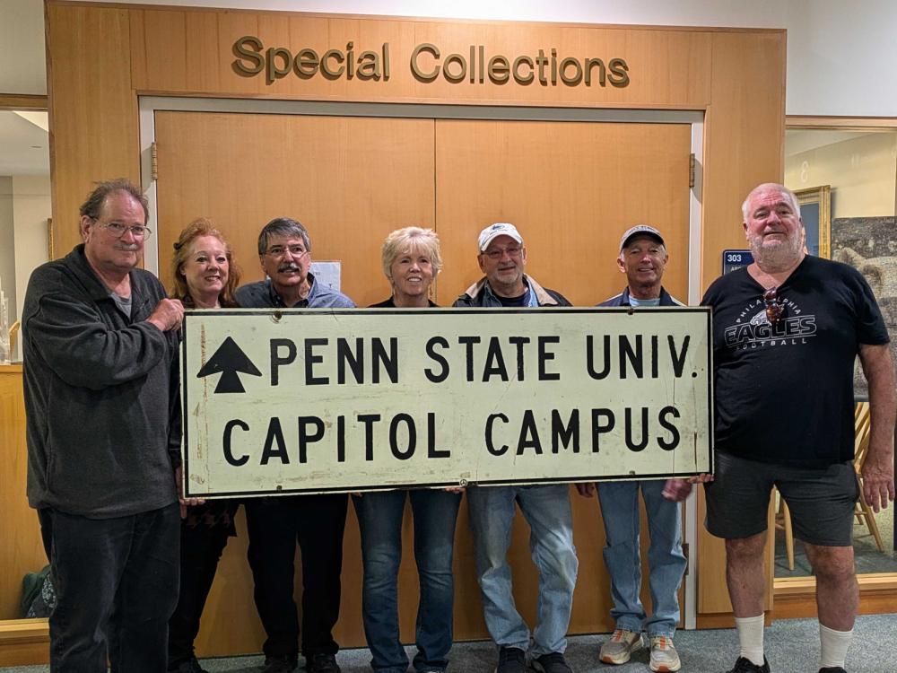 7 Penn State Harrisburg alums and family members pose with a sign that says Penn State Univ. Capitol Campus