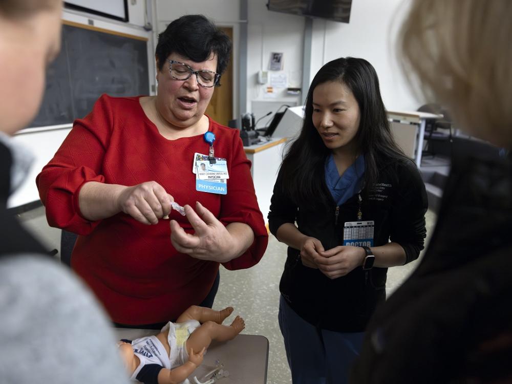 A woman on the left holds a feeding tube and teaches a group of surgical residents.