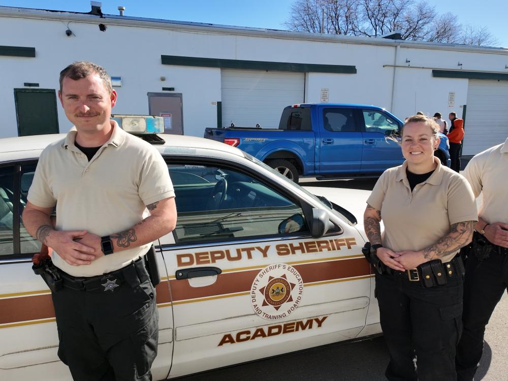 Three people standing in front of a deputy sheriff academy vehicle