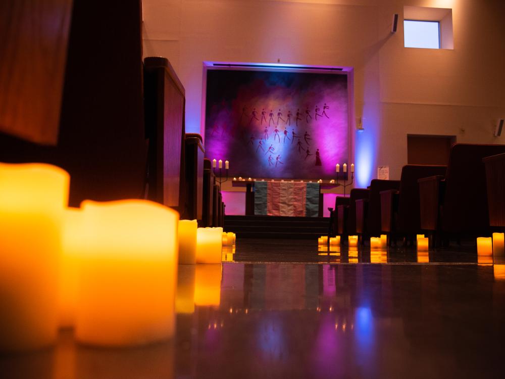 Candles line tables leading up to a dais and tapestry in a dimly lit gathering room