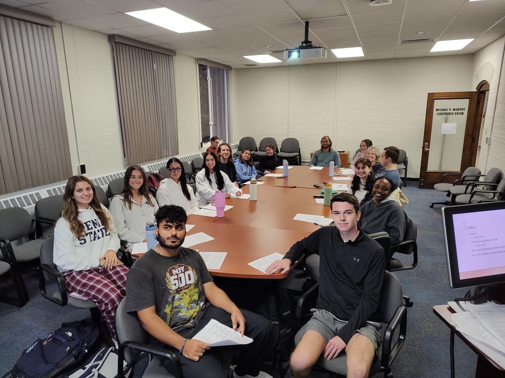 A group of students sitting around a conference table looking at the camera.