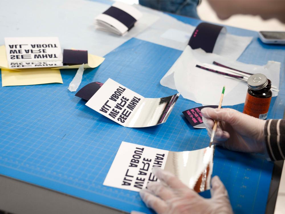 A blue drafting table with invitations atop that are being put together by hand.