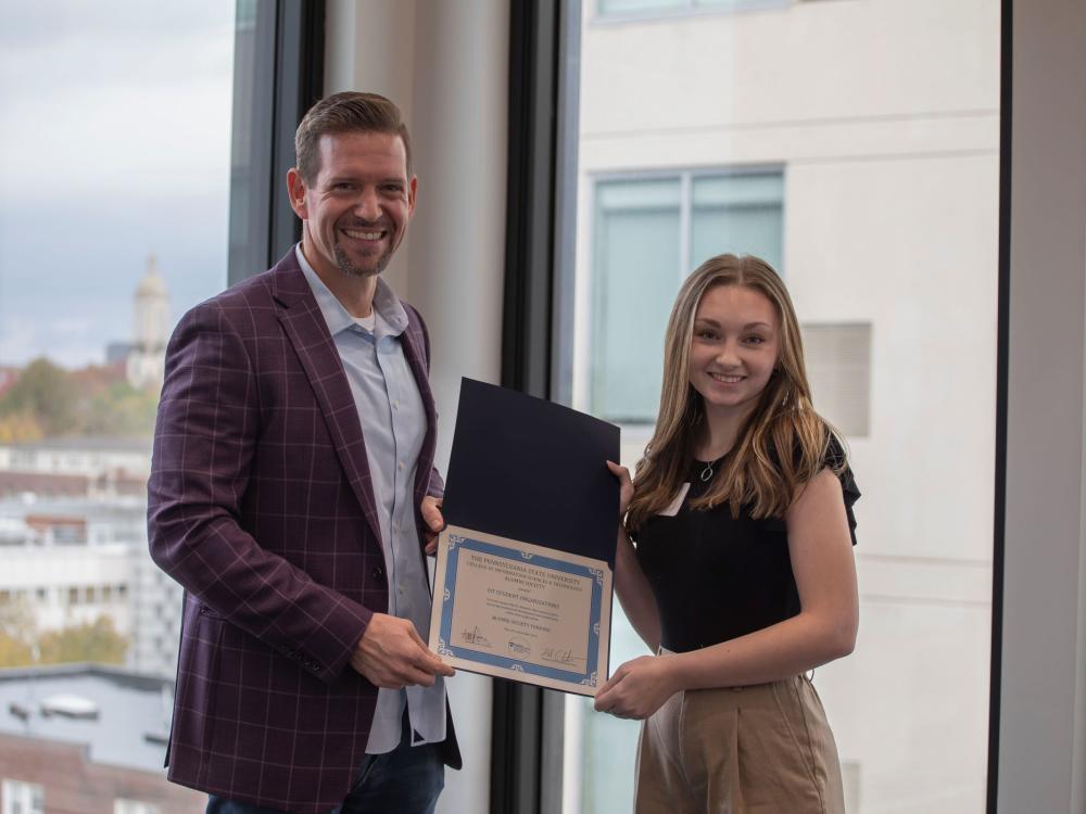 person in suit jacket and beard presents certificate to college student