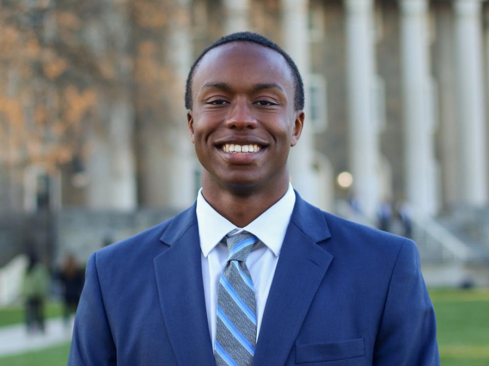 David Hayes stands in a blue suit in front of Old Main at Penn State University Park.
