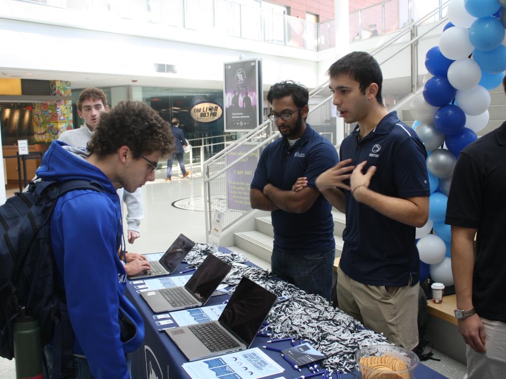 students standing behind a table talking with another student 