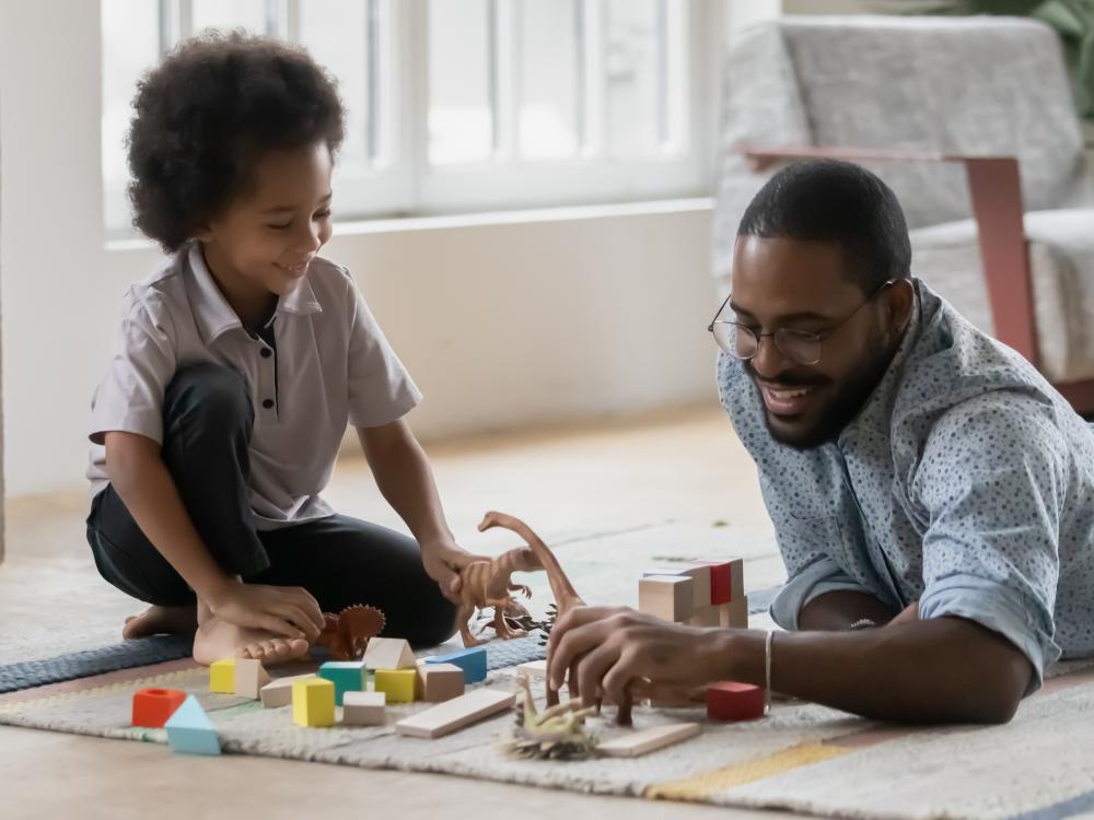 Family spend time together enjoy playtime in cozy living room, young caring father teach little kid play with son using wooden colorful block and dinosaur set toys on warm floor at modern home.