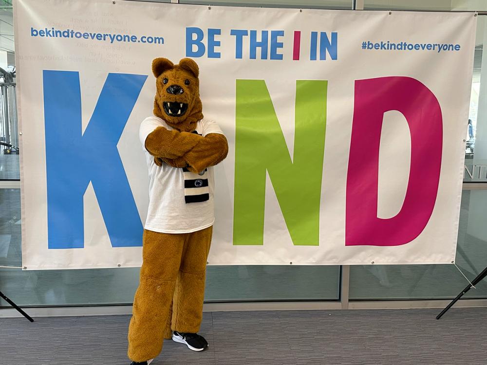 Nittany Lion mascot standing in front of a sign that says Be the I in KIND