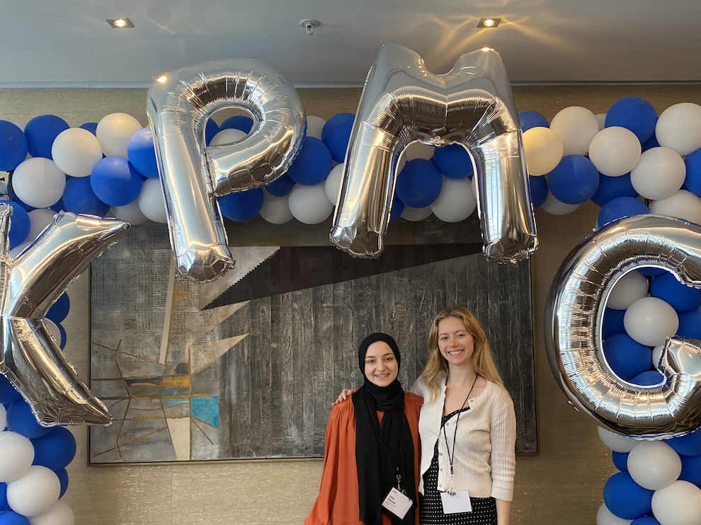 Jessica Krieger (right) stands with another KPMG intern below a blue and white balloon arch with silver balloons that spell out KPMG.