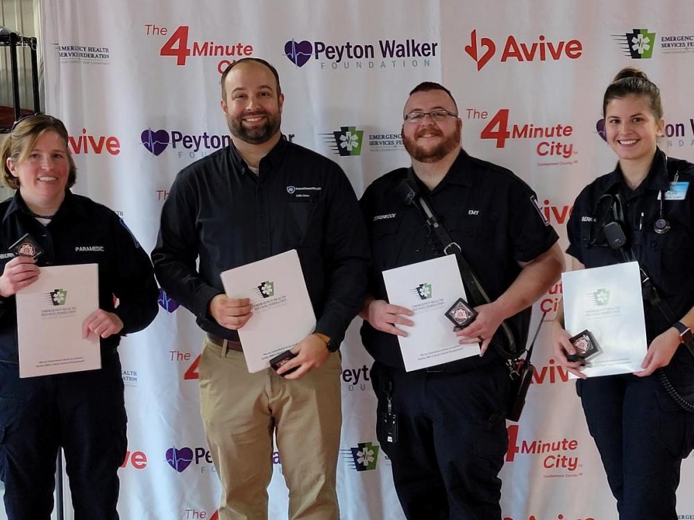 Four people pose for a photograph, each holding in front of them certificates of recognition.