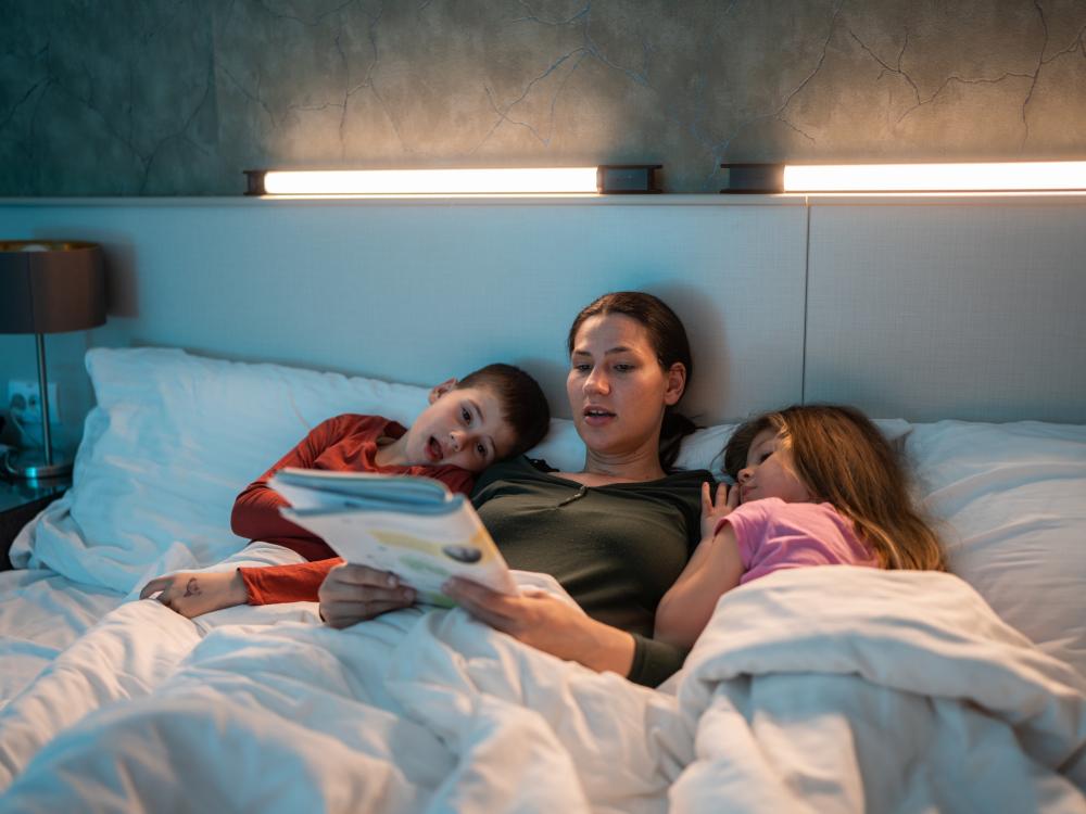 Mother in bed with her two young children, reading a book