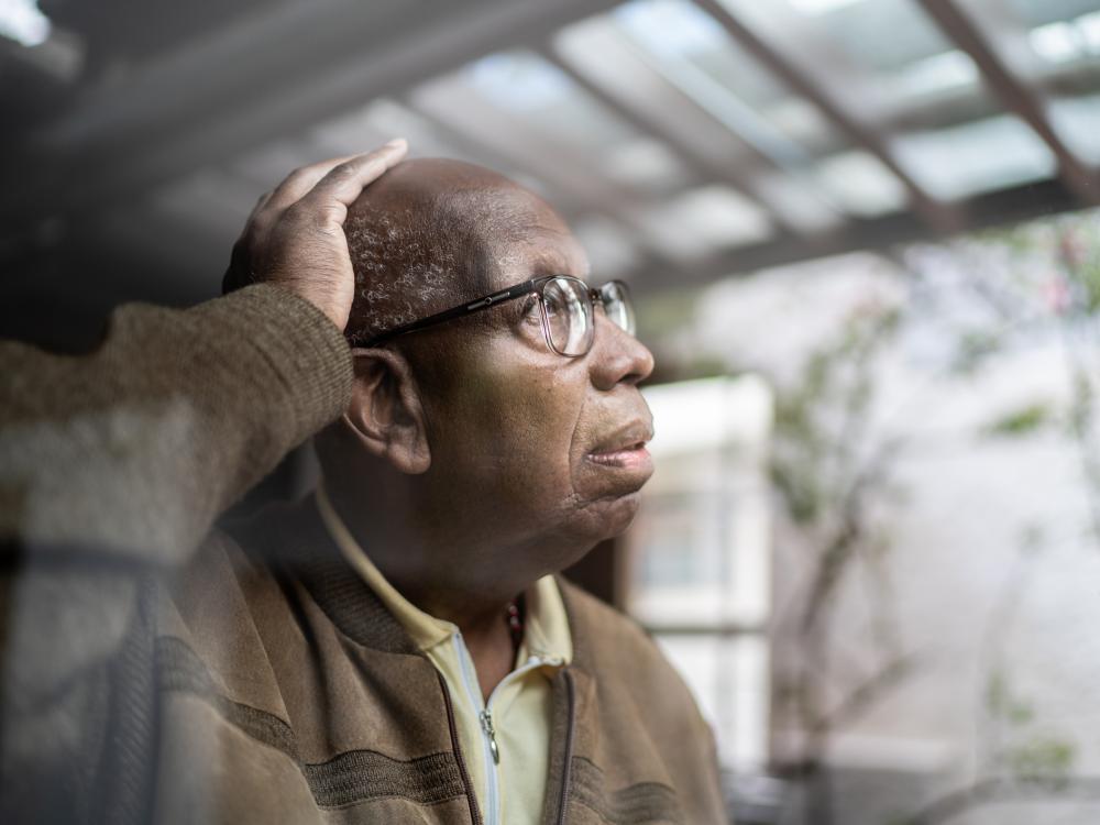 Older man looks concerned as he peers out of his window