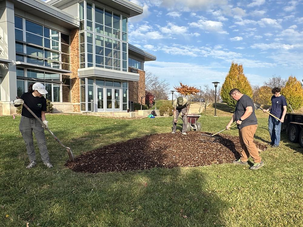 Four people work with shovels and rakes to prepare an area of mulch.