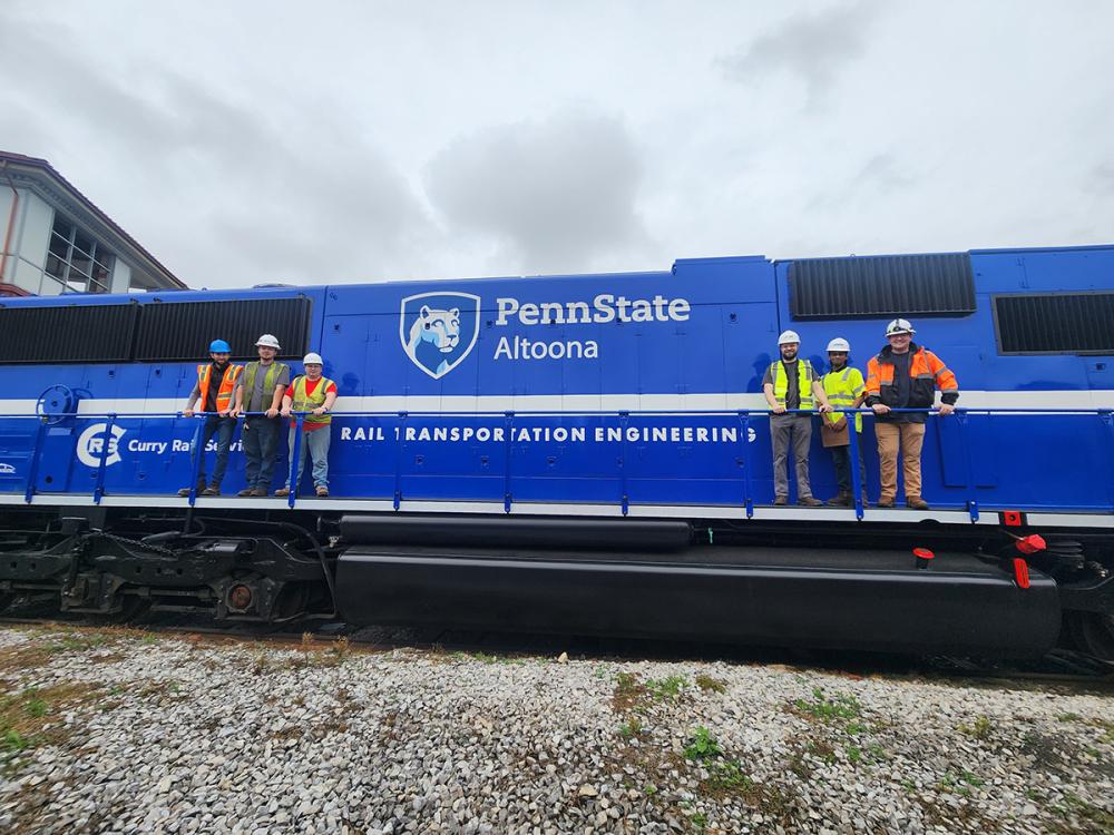 Rail Transportation Engineering students and faculty pose with a Penn State-branded locomotive