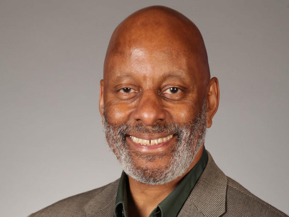 Bald man in a brown suit coat and black dress shirt