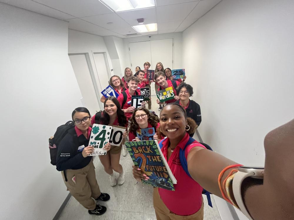 Orientation leader taking selfie in a hallway with 13 others