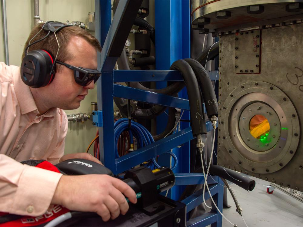 Individual wearing safety goggles and ear protection uses lab equipment. 