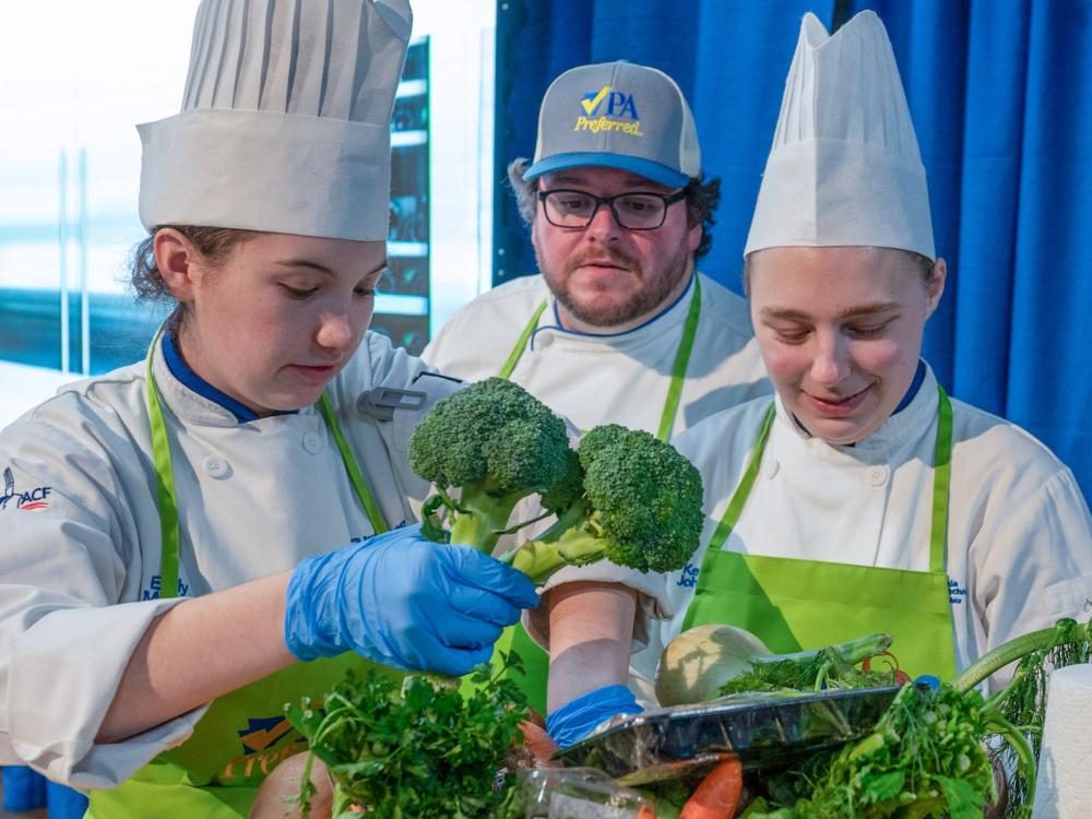 Three chefs look into a basket of produce