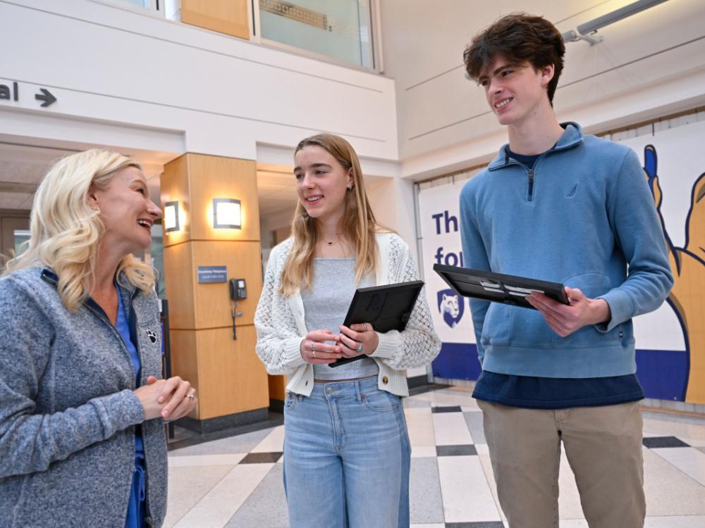 A female nurse speaks to a female and male high school student. The students are holding awards for performing life-saving actions. 