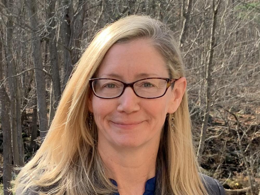 A blonde woman with glasses looks at the camera with a smile.