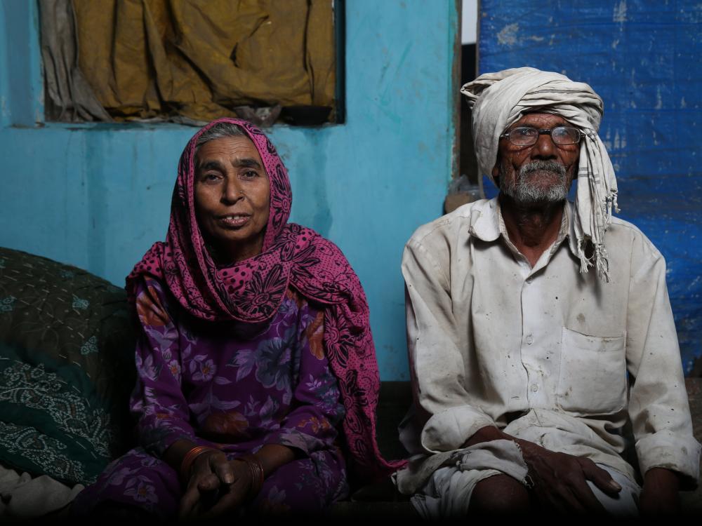 Older person with scarf on head and older person with head covering sit in their modest home