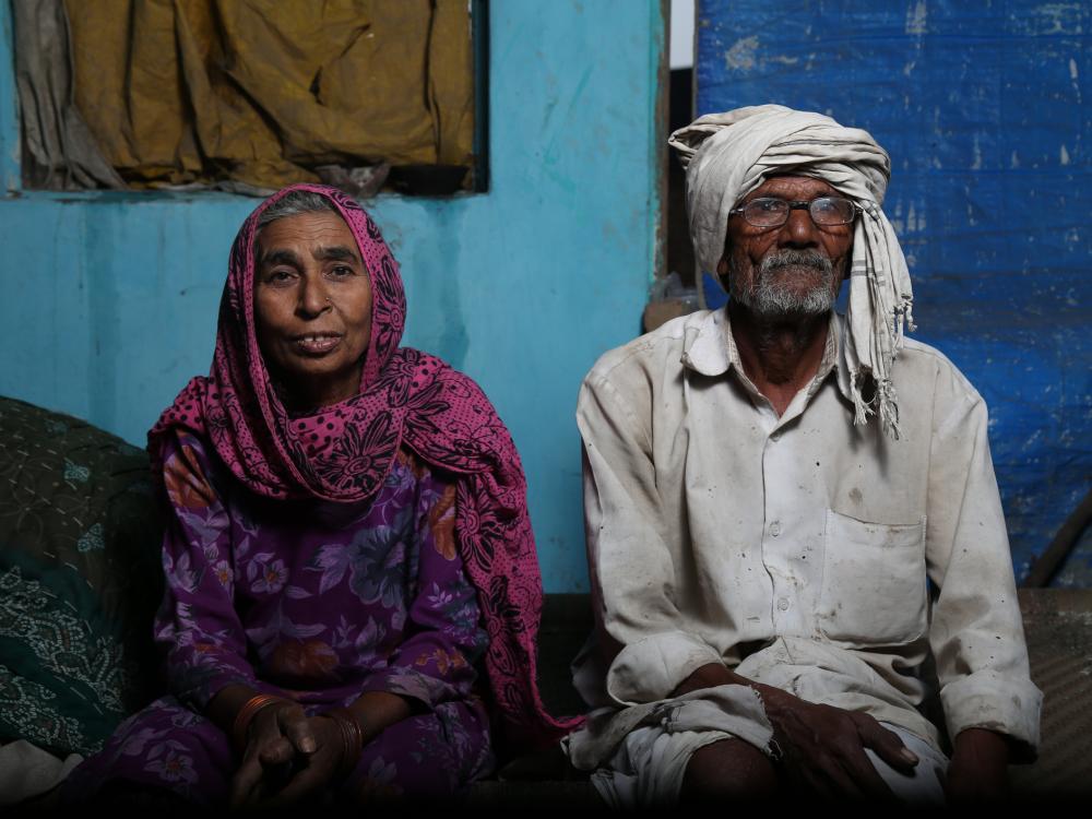 Older person with scarf on head and older person with head covering sit in their modest home