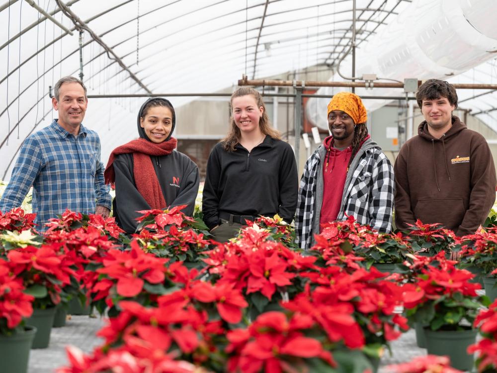 Five individuals gather around red flowers in a Penn College greenhouse.