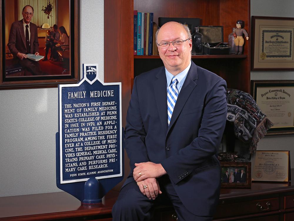 Dr. Mack Ruffin IV sits for a professional portrait next to an historical marker about the nation's first Department of Family Medicine being established at Penn State College of Medicine in 1967.