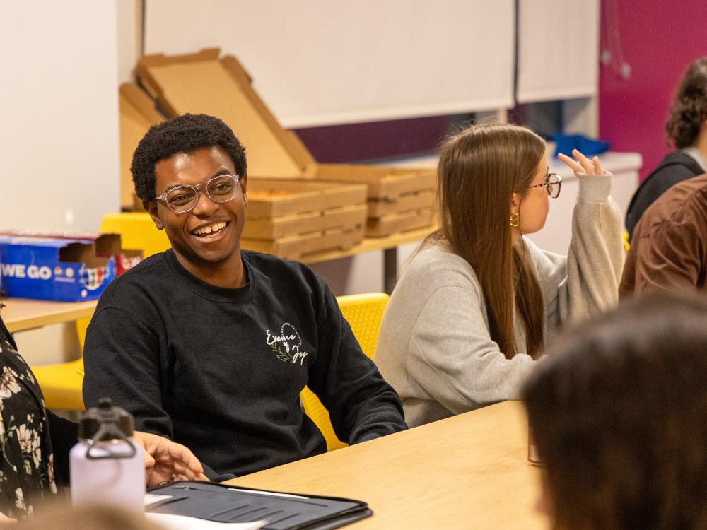 Zion Sykes sits in a chair at a table full of first-year Liberal Arts students while laughing and talking to the group.