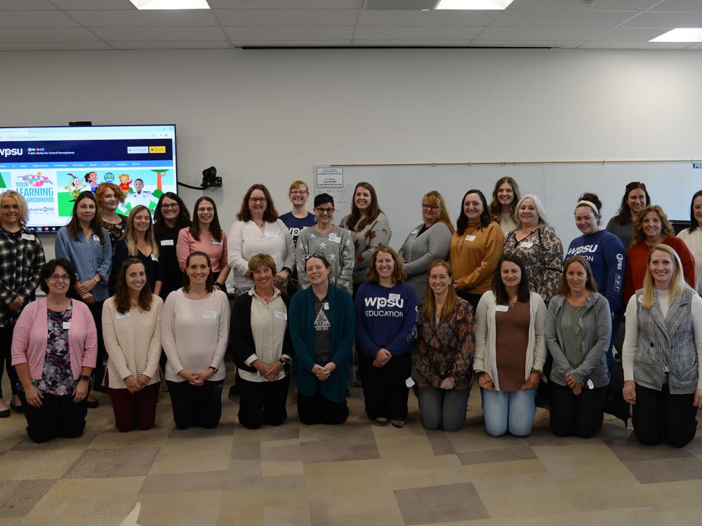 Photo of people standing in two rows in front of a presentation screen.