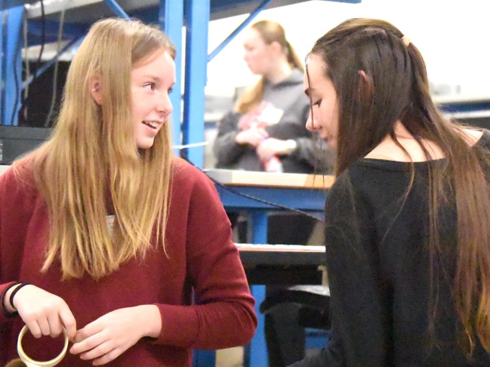 Two high school girls face each other and smile while building a model pipeline out of cardboard tubes.