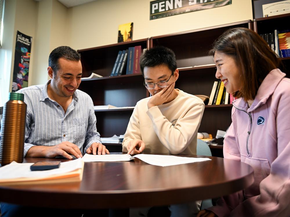 Three people sit around a table with bookshelves in the background