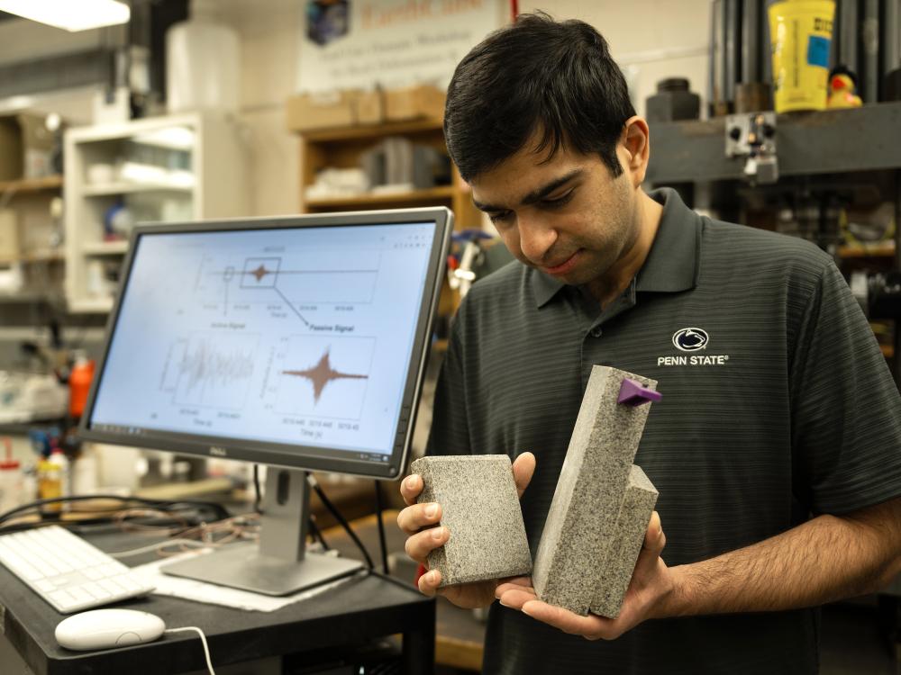 A person standing next to a computer screen holds two rocks. 