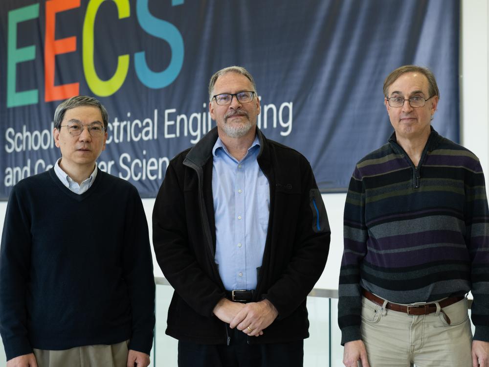 Three people pose outside in front of an electrical engineering and computer science banner.