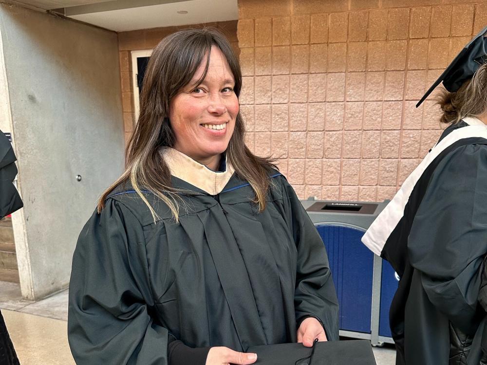 Jenny Brunson smiles in the Bryce Jordan Center dressed in a black cap and gown at Penn State’s fall 2024 commencement ceremony.