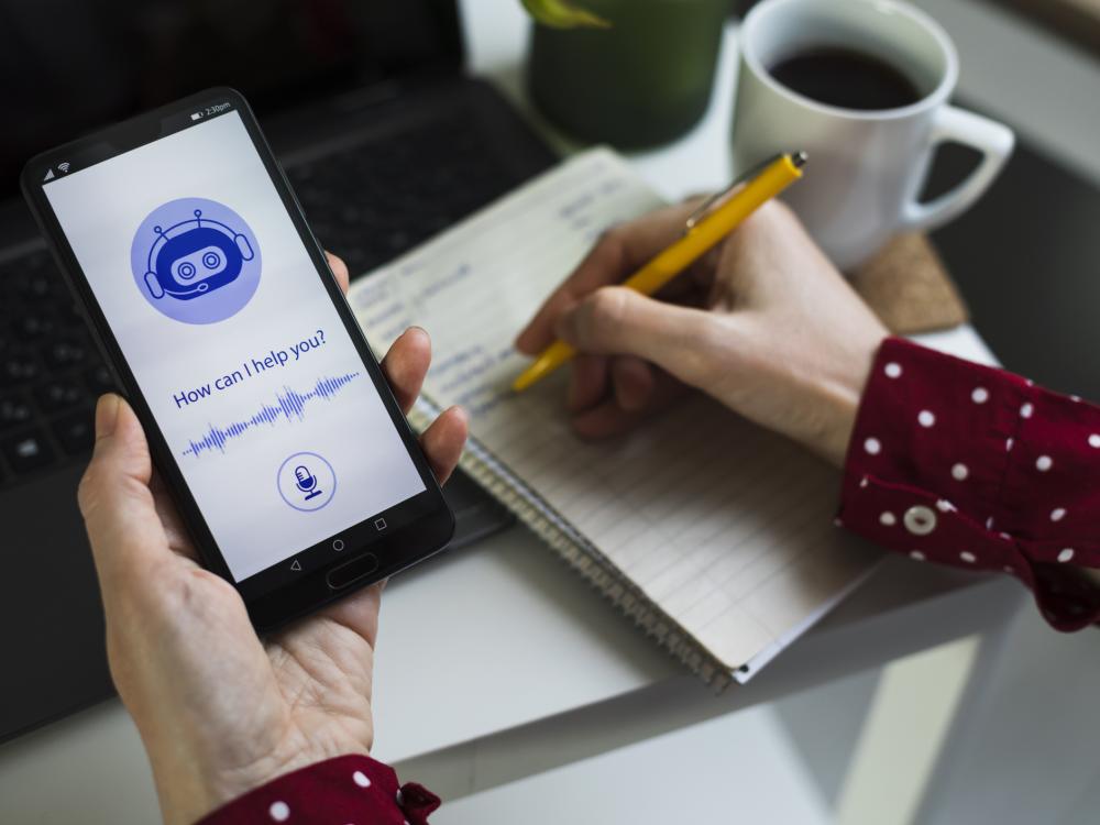 A person holding a smartphone with an AI assistant on the screen asking, "How can I help you?"