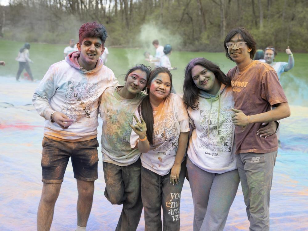 Five students covered in colorful dust smile for the camera.