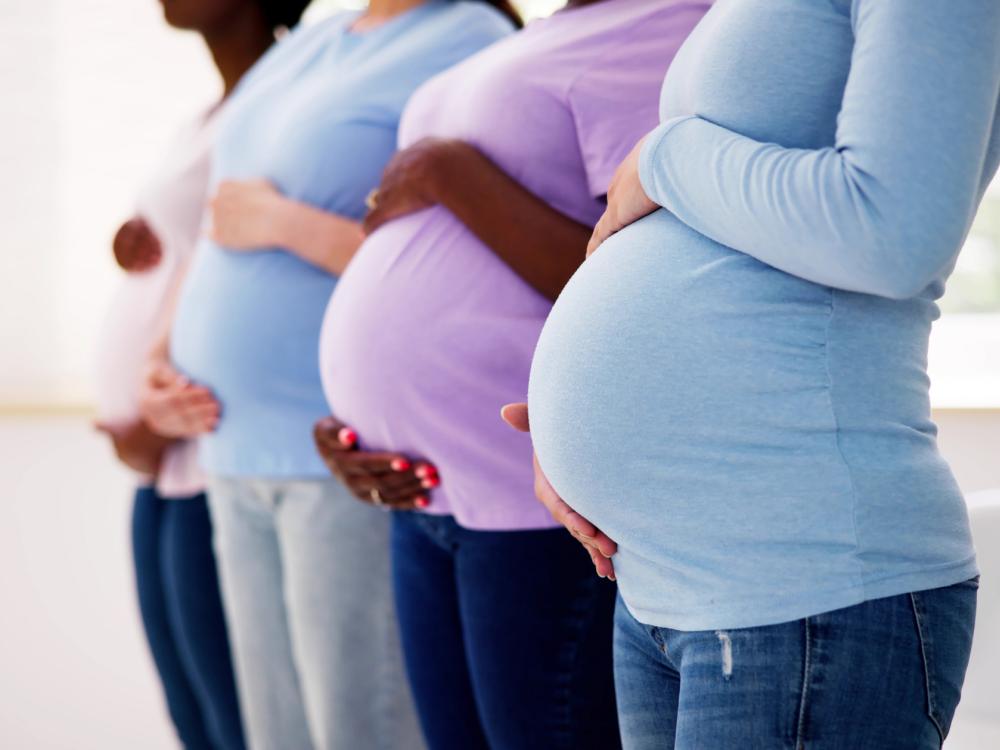 Four pregnant women in a line wearing casual clothes, shown from mid-thigh to neck