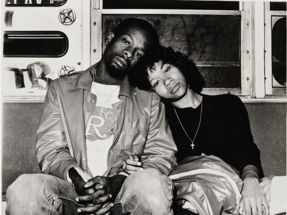 Photo of a seated Black couple leaning against each other on a subway train