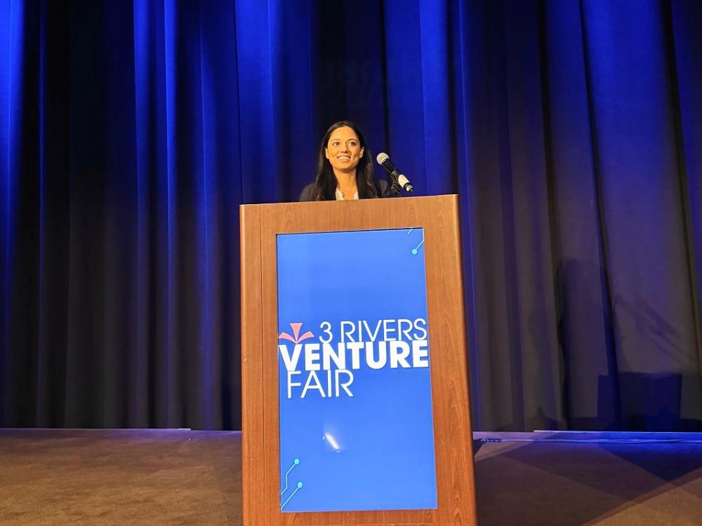 A woman stands at a podium on a stage, pitching a business idea.