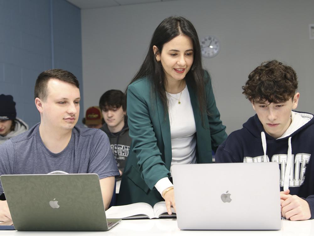 Professor Dima Rabadi works with students on laptops